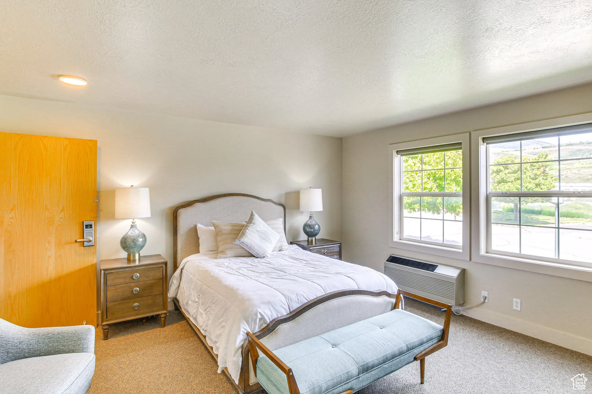 Carpeted bedroom with a textured ceiling and a wall mounted AC