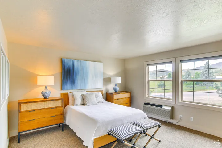 Bedroom with carpet, a textured ceiling, and an AC wall unit