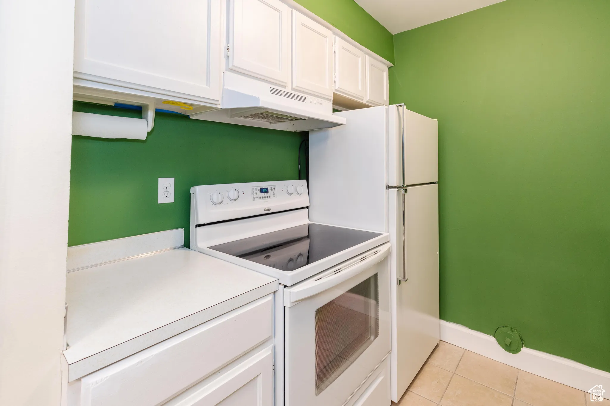 Kitchen with white appliances, white cabinets, light tile patterned floors, under cabinet range hood, and light countertops