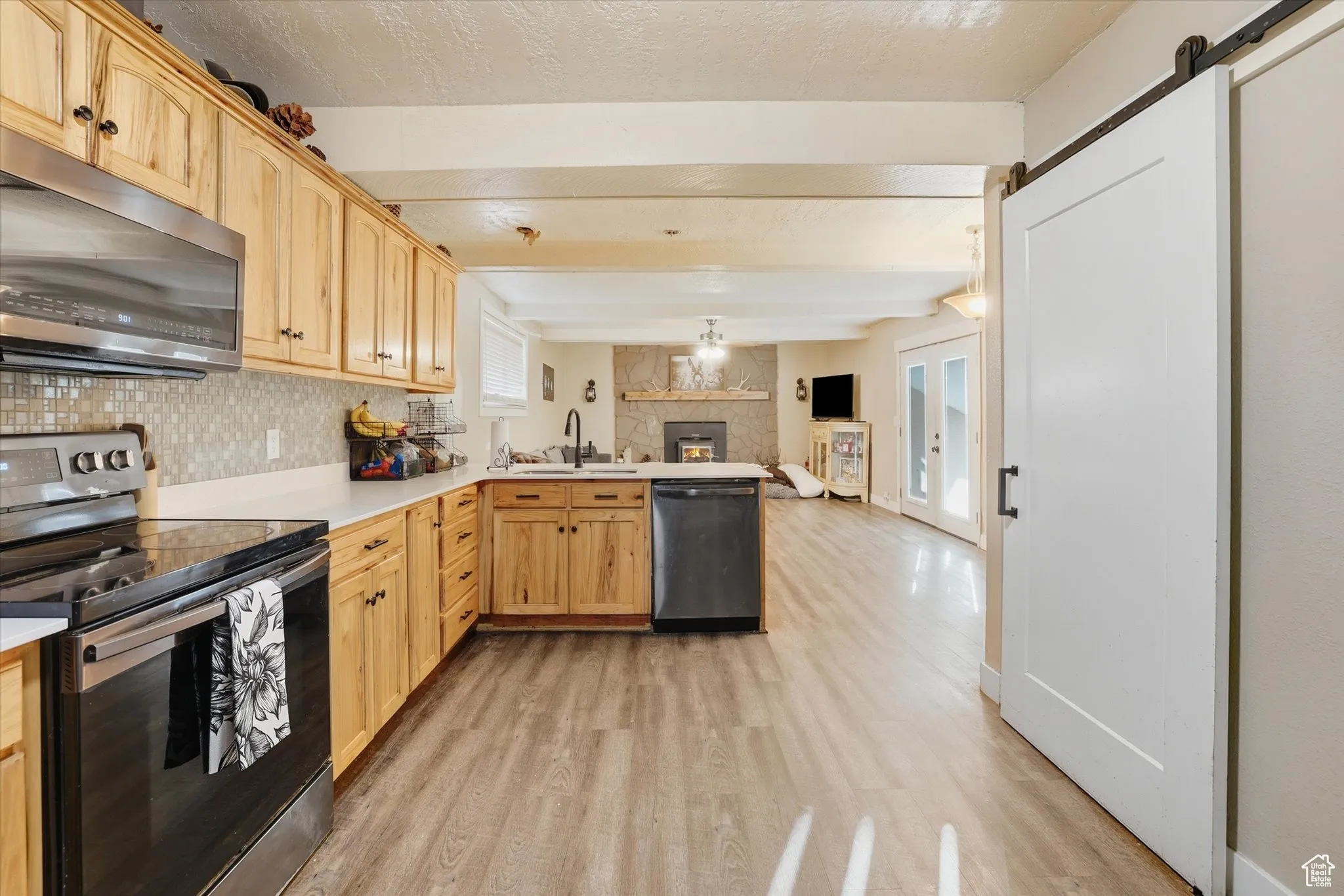 Kitchen featuring a barn door, appliances with stainless steel finishes, light countertops, light wood-type flooring, and beam ceiling