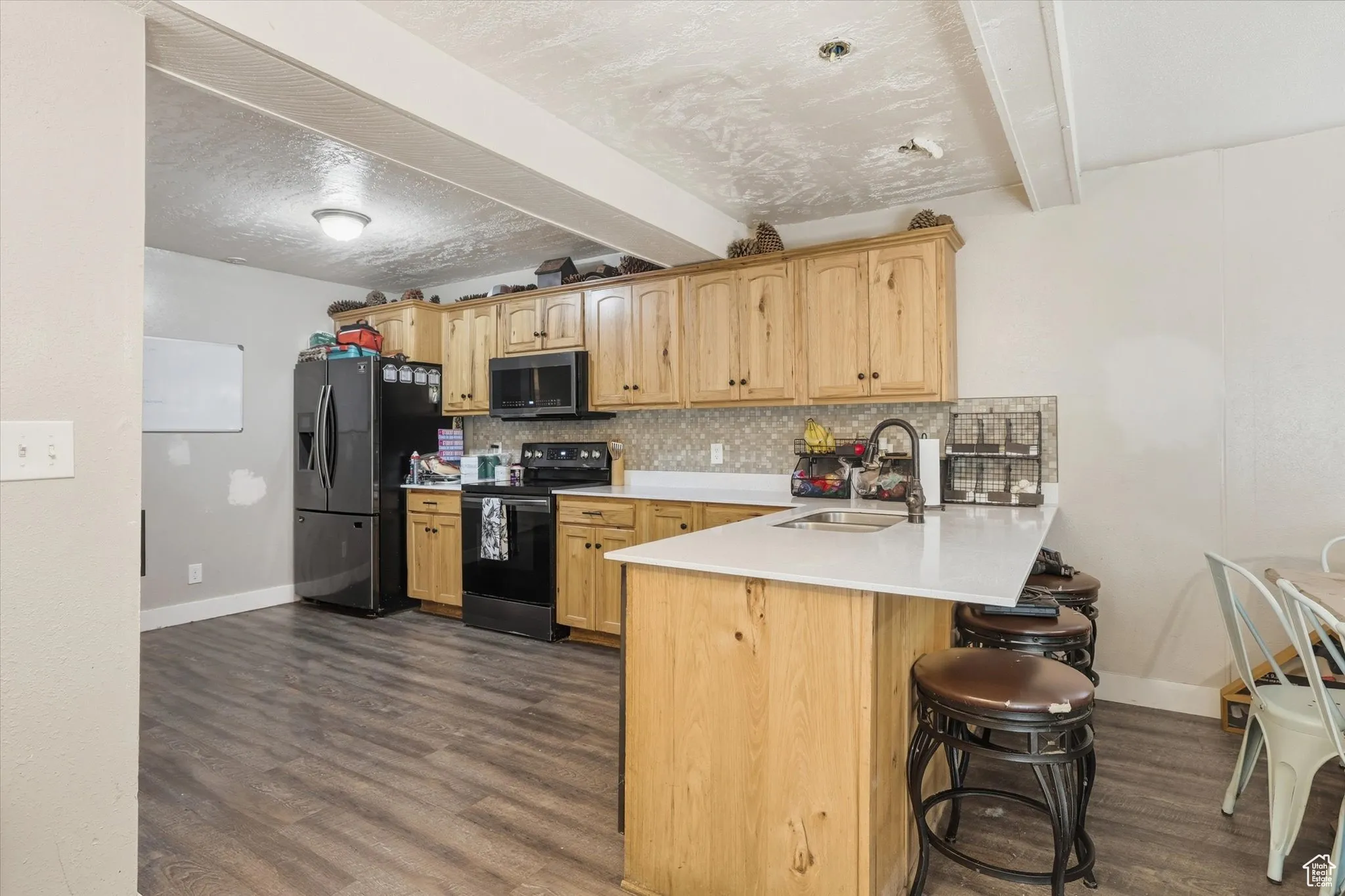 Kitchen featuring black range with electric cooktop, beam ceiling, backsplash, a kitchen bar, and stainless steel fridge with ice dispenser