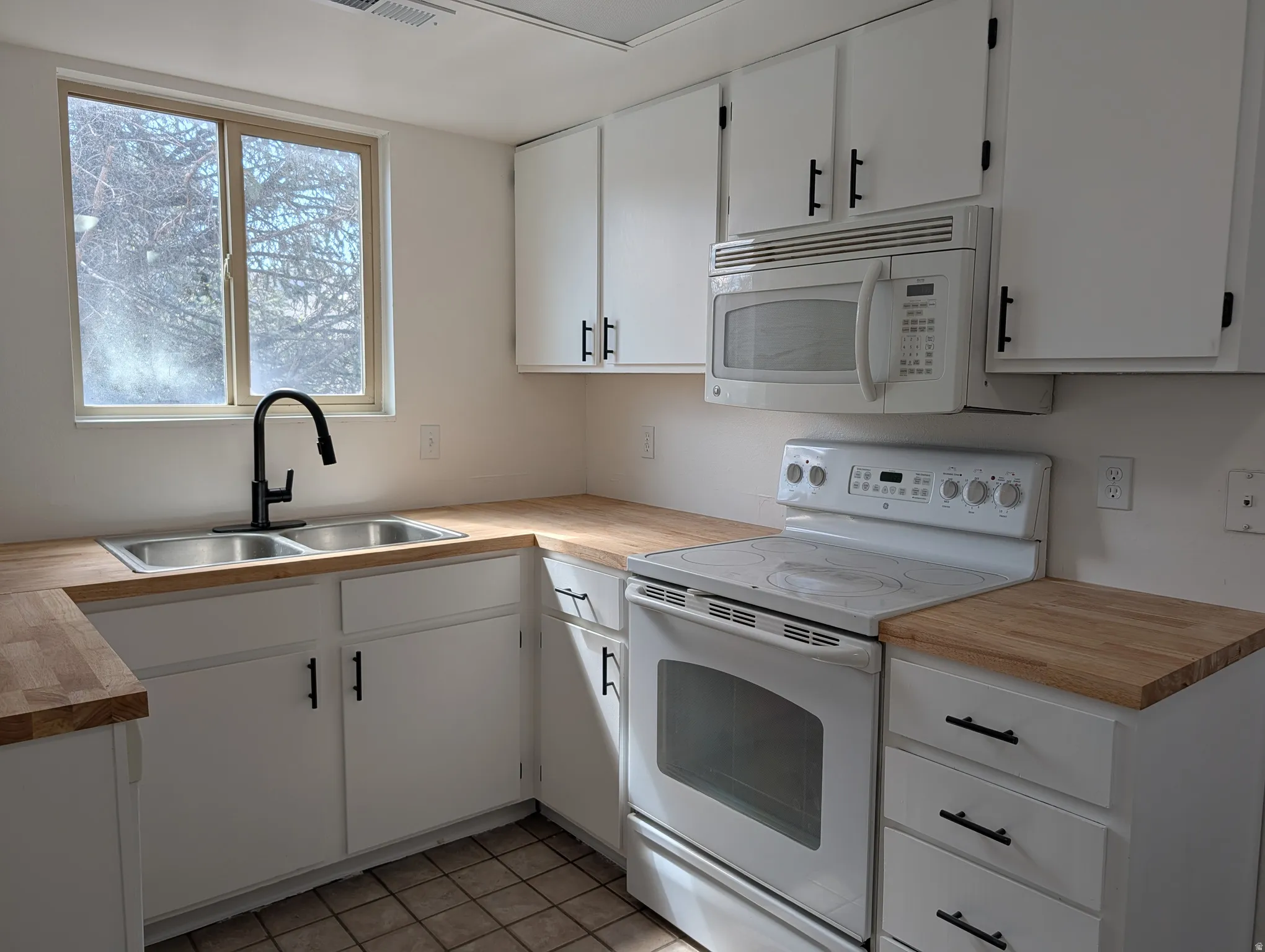 Kitchen featuring white appliances, white cabinetry, butcher block countertops, and light tile patterned floors
