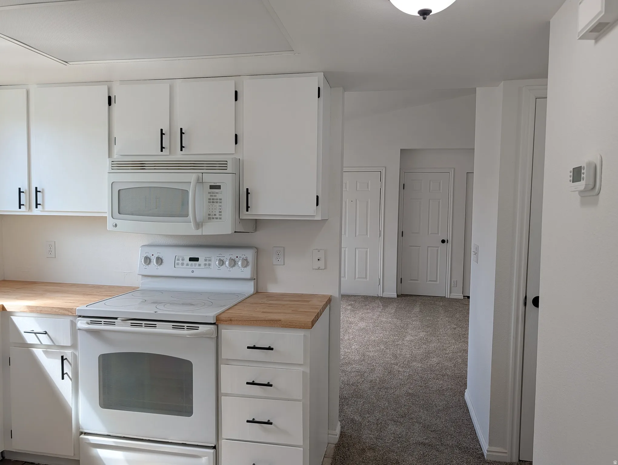 Kitchen with white cabinets, white appliances, light carpet, and butcher block countertops