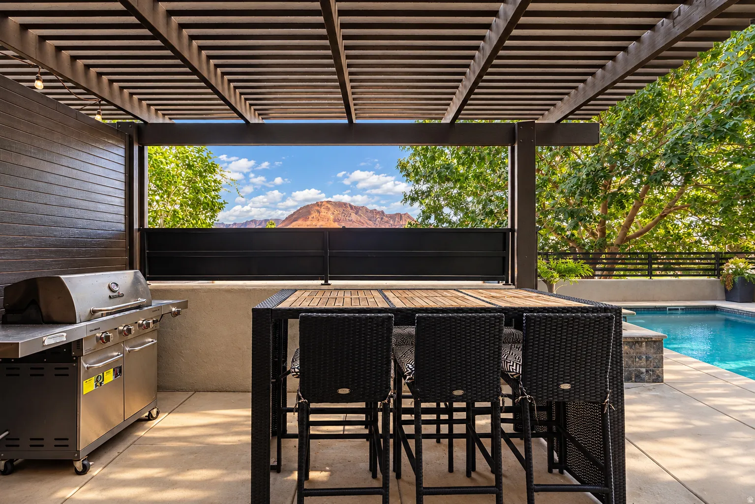 Covered patio with slatted ceiling, built-in outdoor kitchen with stainless steel grill, concrete patio, and in-ground pool
