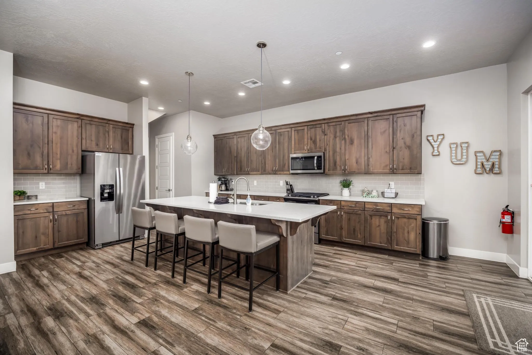 Kitchen with a kitchen breakfast bar, appliances with stainless steel finishes, decorative backsplash, hanging light fixtures, and an island with sink