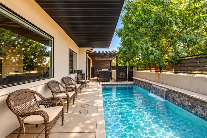 Outdoor living space featuring a swimming pool with a waterfall, an extended patio, an overhead pergola, and a covered patio area