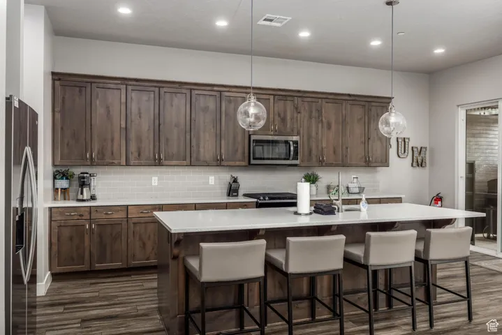 Kitchen featuring appliances with stainless steel finishes, recessed lighting, hanging light fixtures, a center island with sink, and backsplash