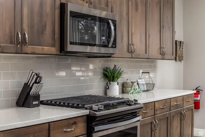 Kitchen featuring stainless steel appliances, decorative backsplash, light stone counters, and dark brown cabinets