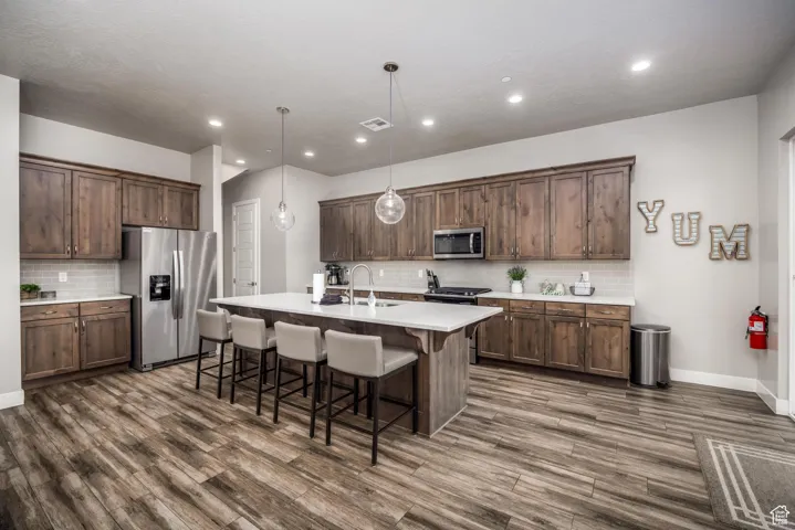 Kitchen with a kitchen breakfast bar, appliances with stainless steel finishes, decorative backsplash, hanging light fixtures, and an island with sink