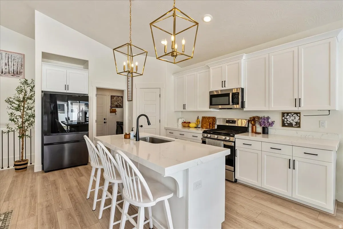 Kitchen with stainless steel appliances, a breakfast bar, a center island with sink, white cabinets, and hanging light fixtures