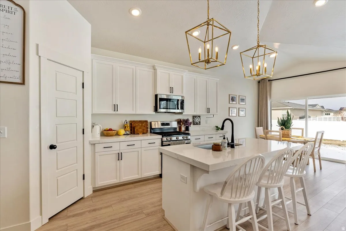 Kitchen featuring an island with sink, appliances with stainless steel finishes, hanging light fixtures, a kitchen bar, and light wood finished floors
