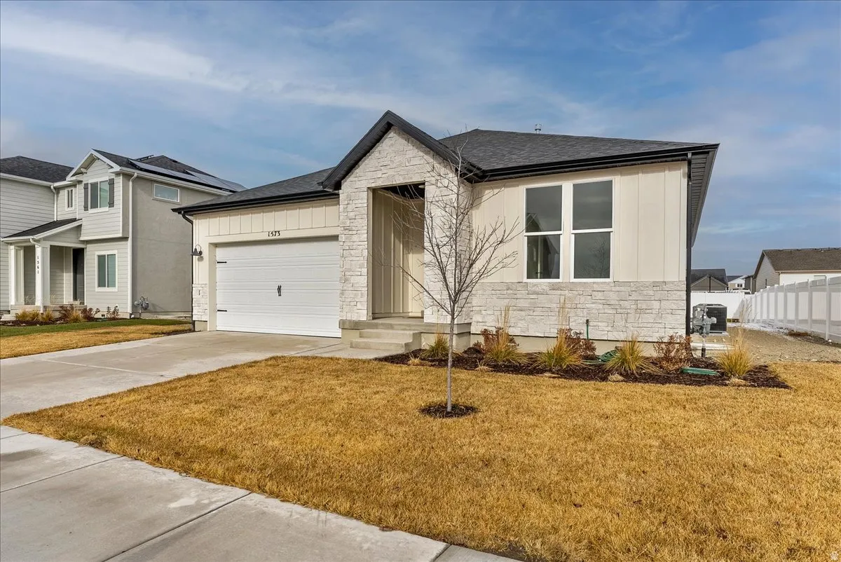 View of front of home featuring stone siding, driveway, a shingled roof, board and batten siding, and a front yard