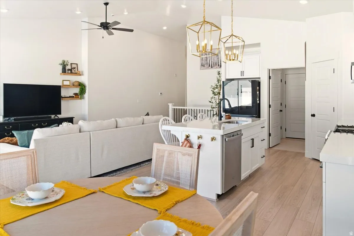 Kitchen featuring open floor plan, white cabinets, an island with sink, pendant lighting, and black refrigerator