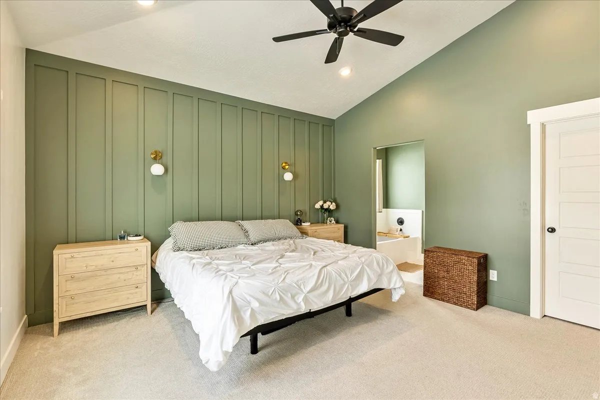 Bedroom with lofted ceiling, a decorative wall, carpet flooring, connected bathroom, and a ceiling fan