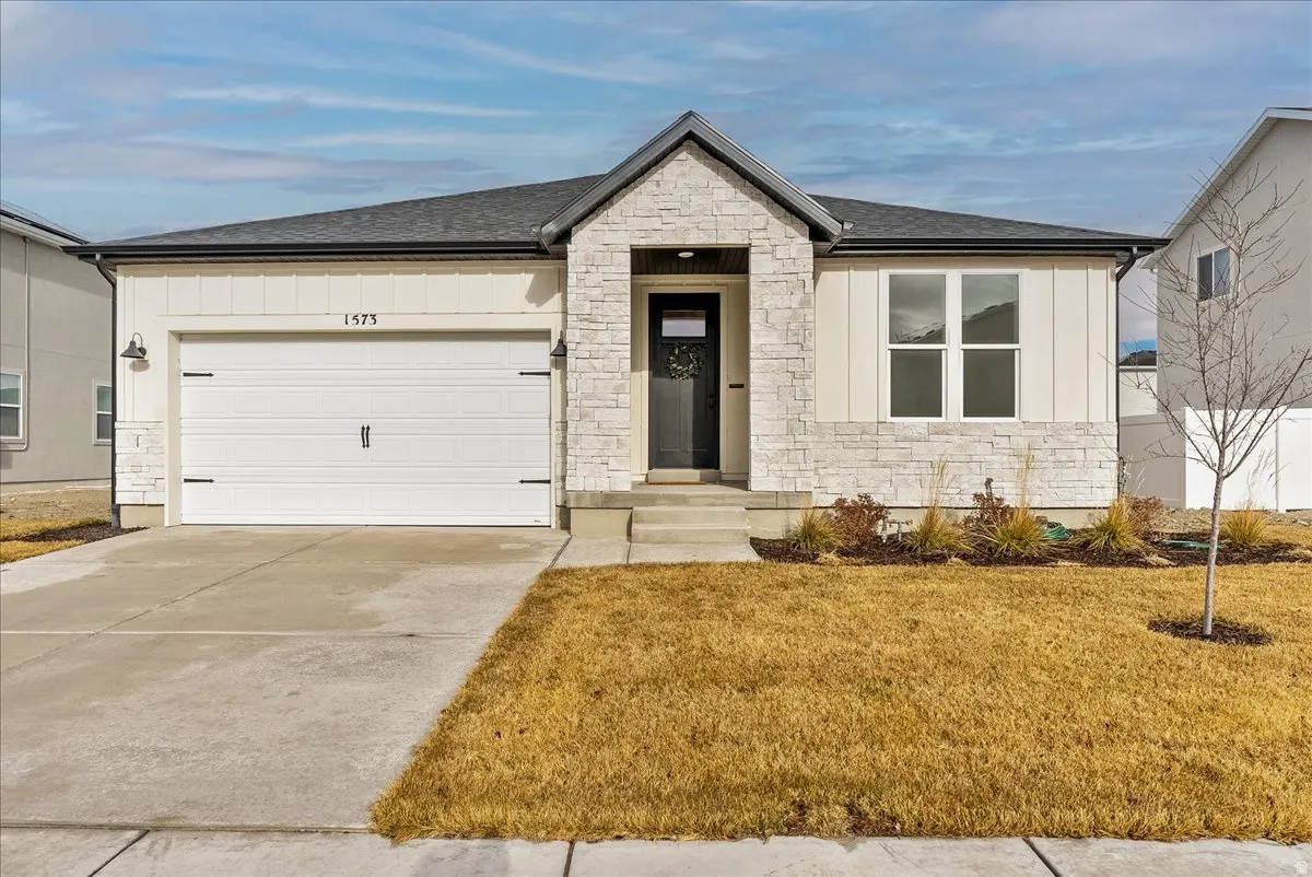View of front of house with stone siding, driveway, and a shingled roof