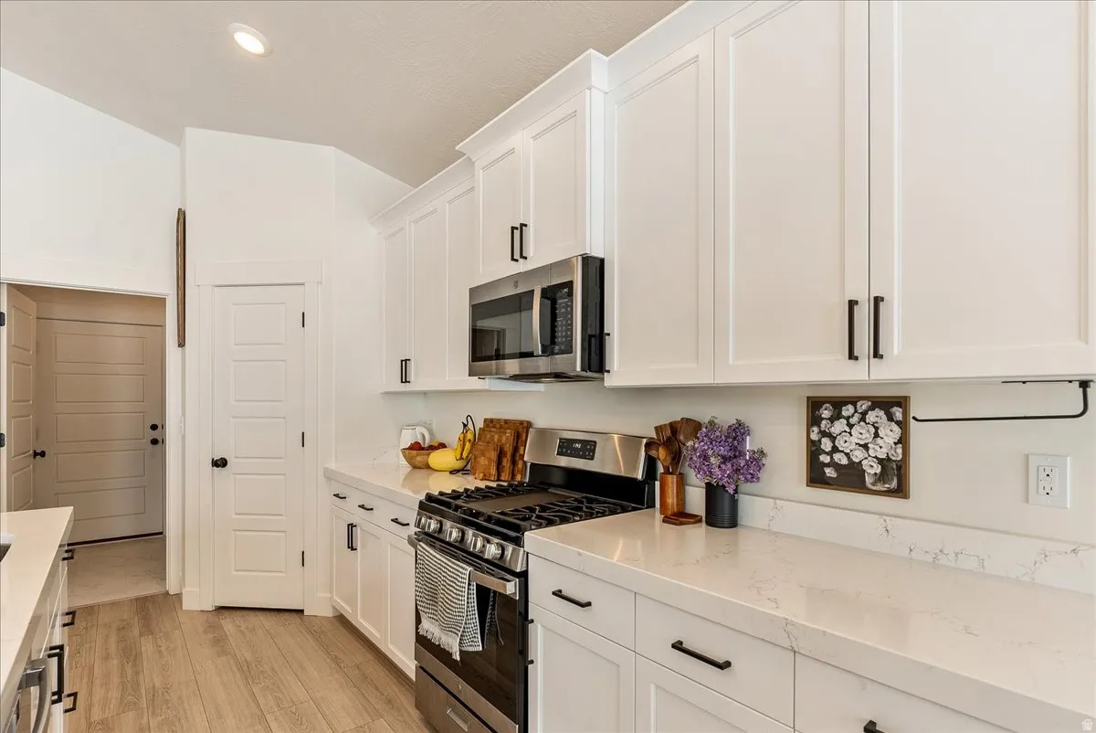 Kitchen with appliances with stainless steel finishes, white cabinetry, light wood-style flooring, light stone countertops, and recessed lighting