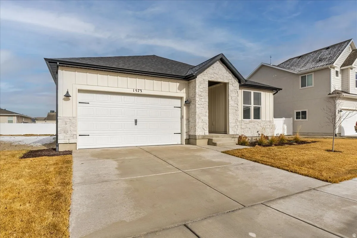 View of front facade featuring stone siding, driveway, an attached garage, a shingled roof, and board and batten siding