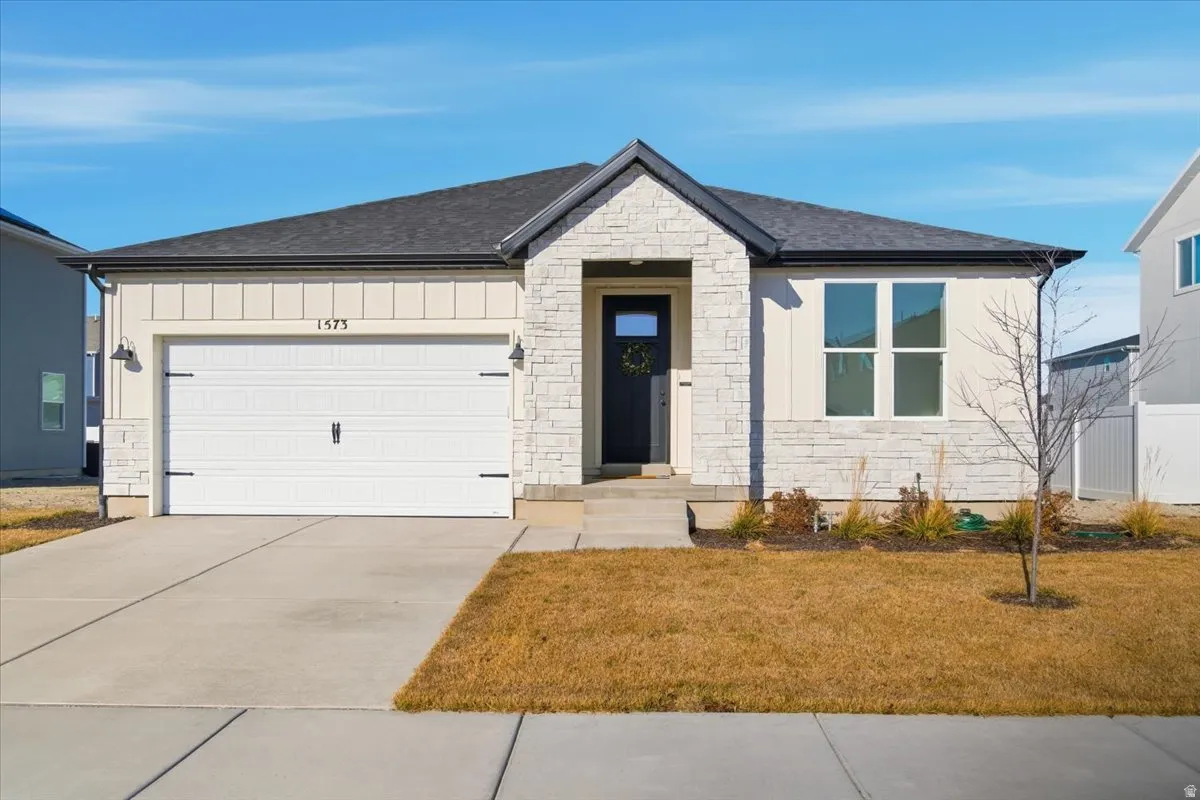 View of front facade with stone siding, concrete driveway, a garage, a shingled roof, and a front lawn
