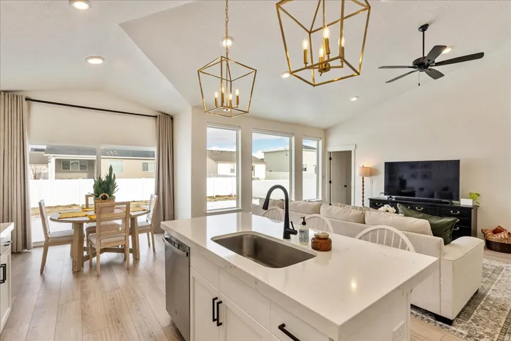 Kitchen with vaulted ceiling, white cabinetry, decorative light fixtures, light wood finished floors, and light stone countertops