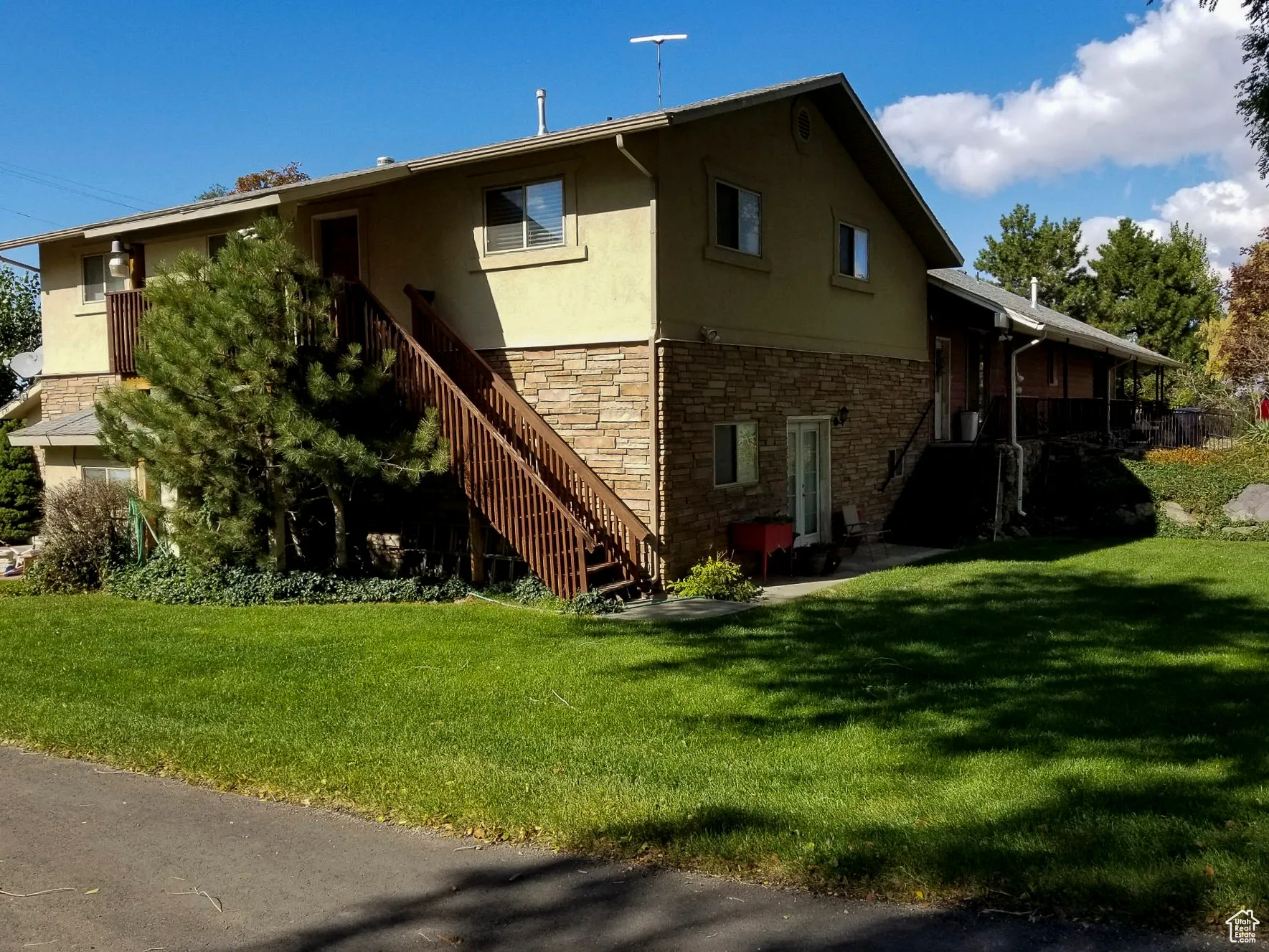 Back of property featuring stone siding, stucco siding, a lawn, and stairs
