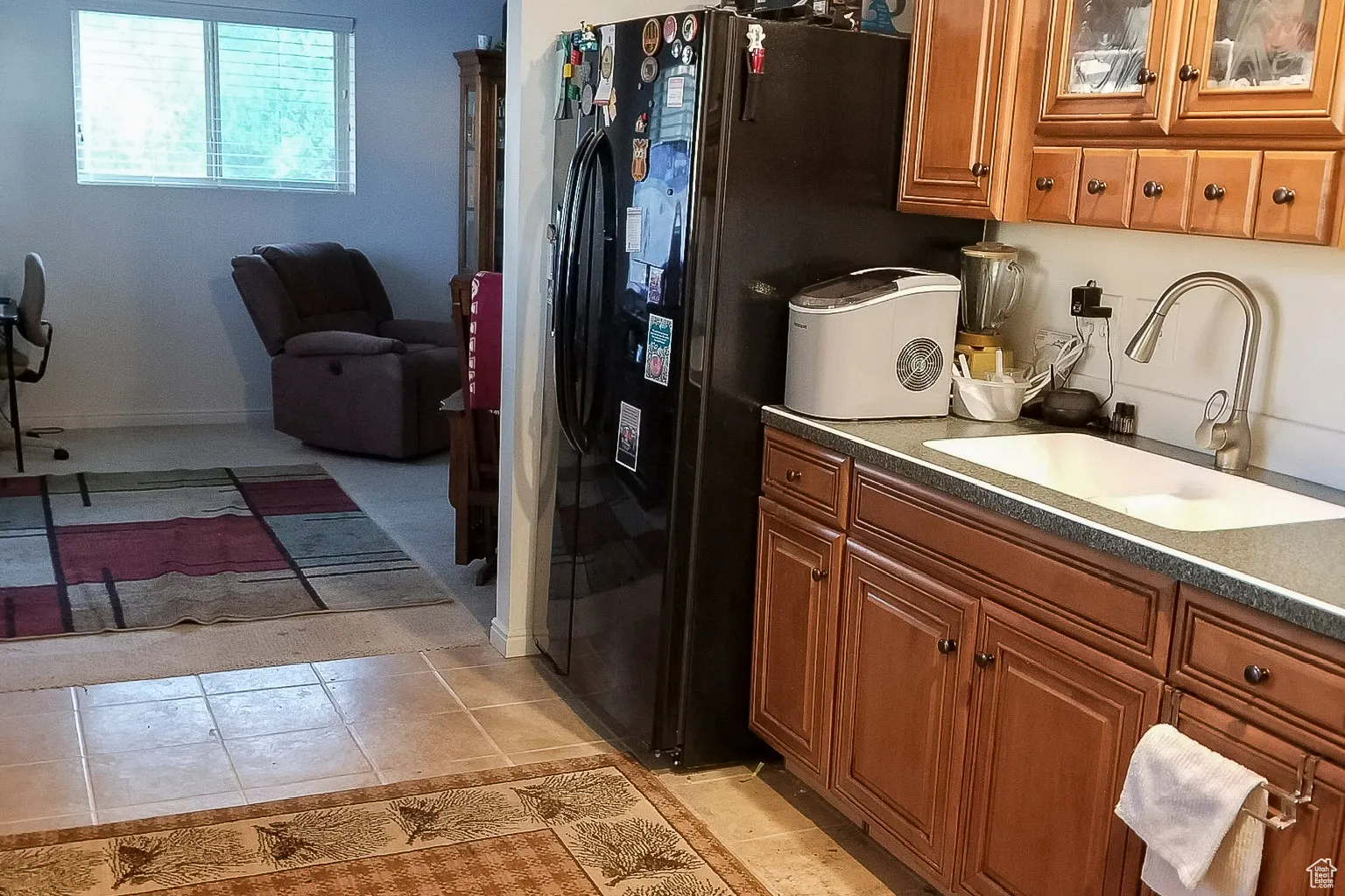 Kitchen featuring brown cabinetry, black refrigerator with ice dispenser, light tile patterned flooring, and dark stone countertops