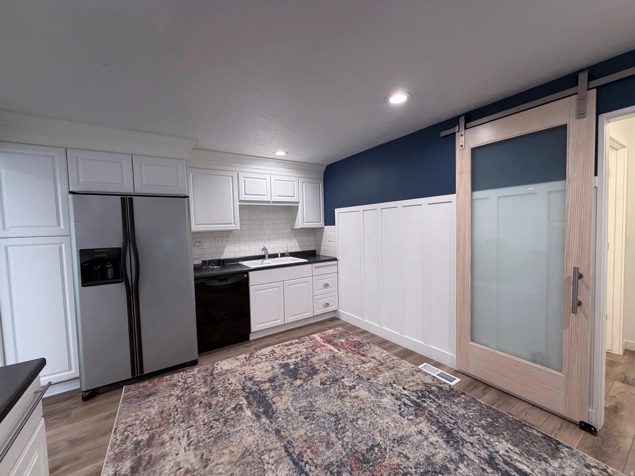 Kitchen featuring a barn door, white cabinets, dark countertops, stainless steel fridge, and dishwasher