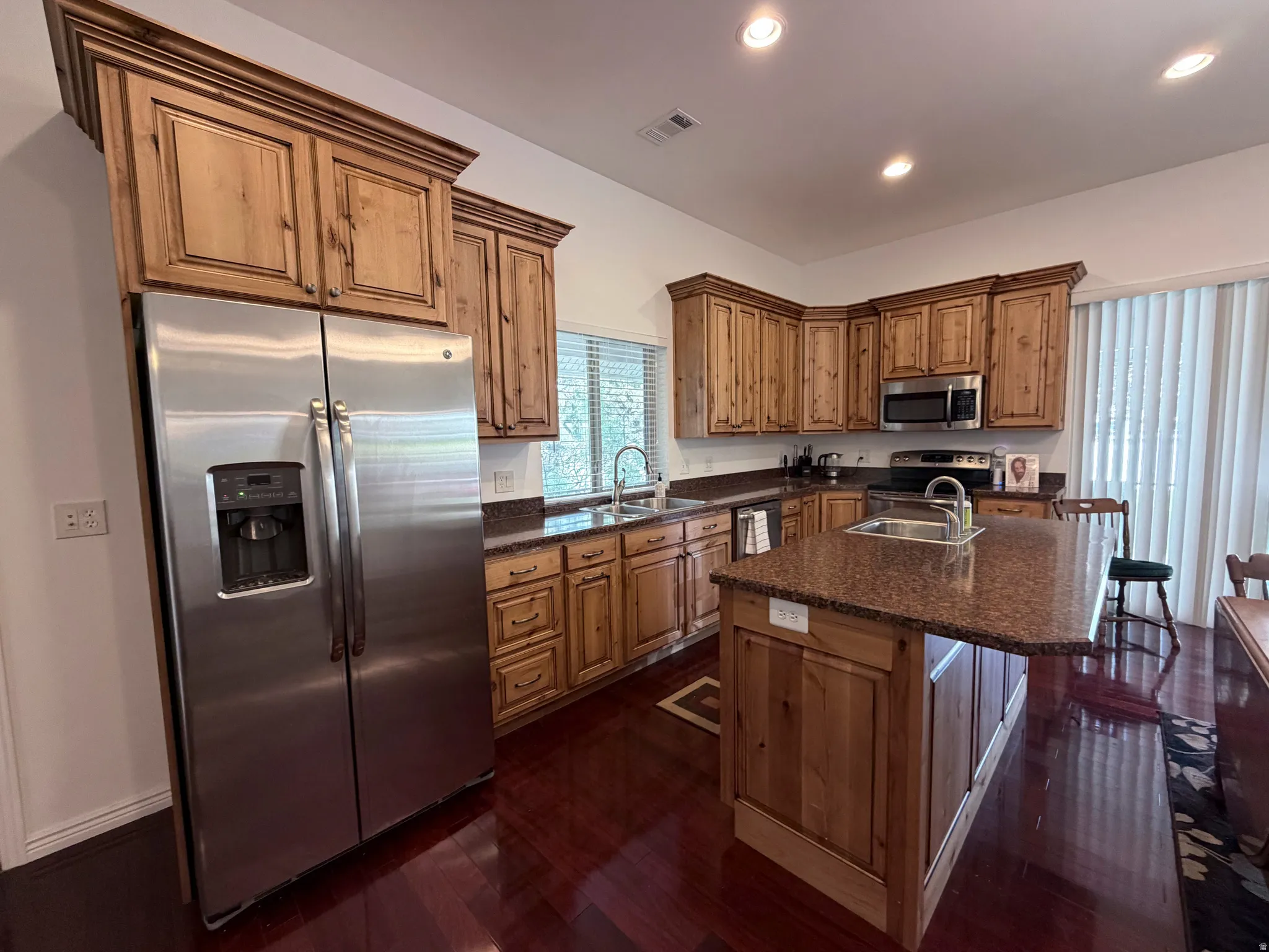 Kitchen with stainless steel appliances, a center island with sink, a kitchen bar, dark wood-style floors, and recessed lighting