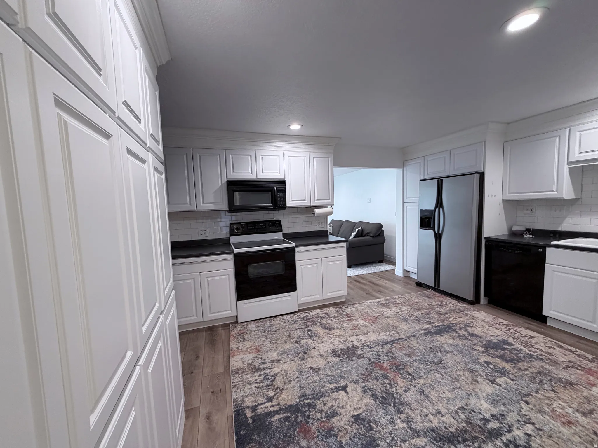 Kitchen with black appliances, white cabinetry, light wood-style flooring, tasteful backsplash, and recessed lighting