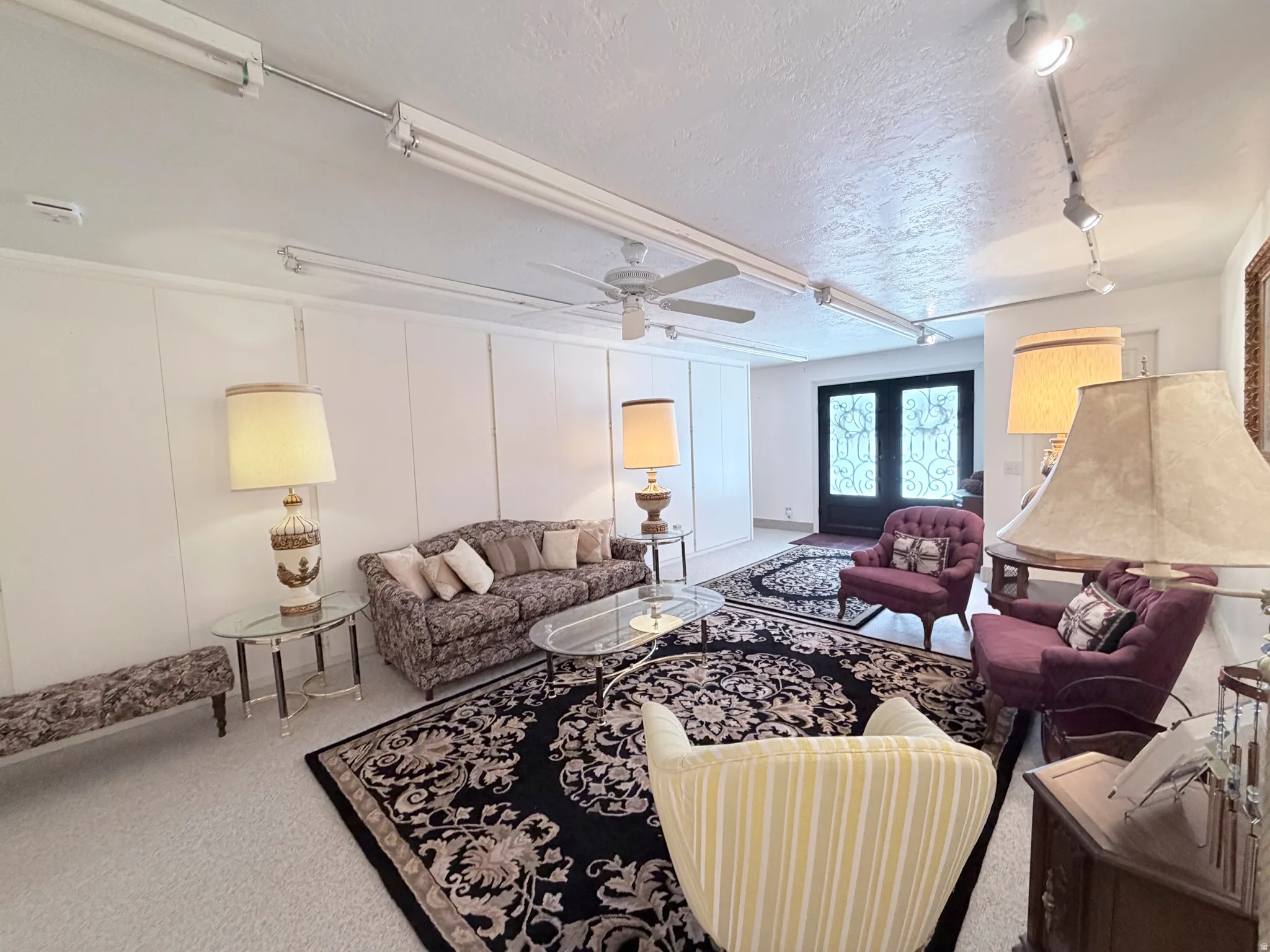 Living room with a decorative wall, a textured ceiling, french doors, carpet, and ceiling fan