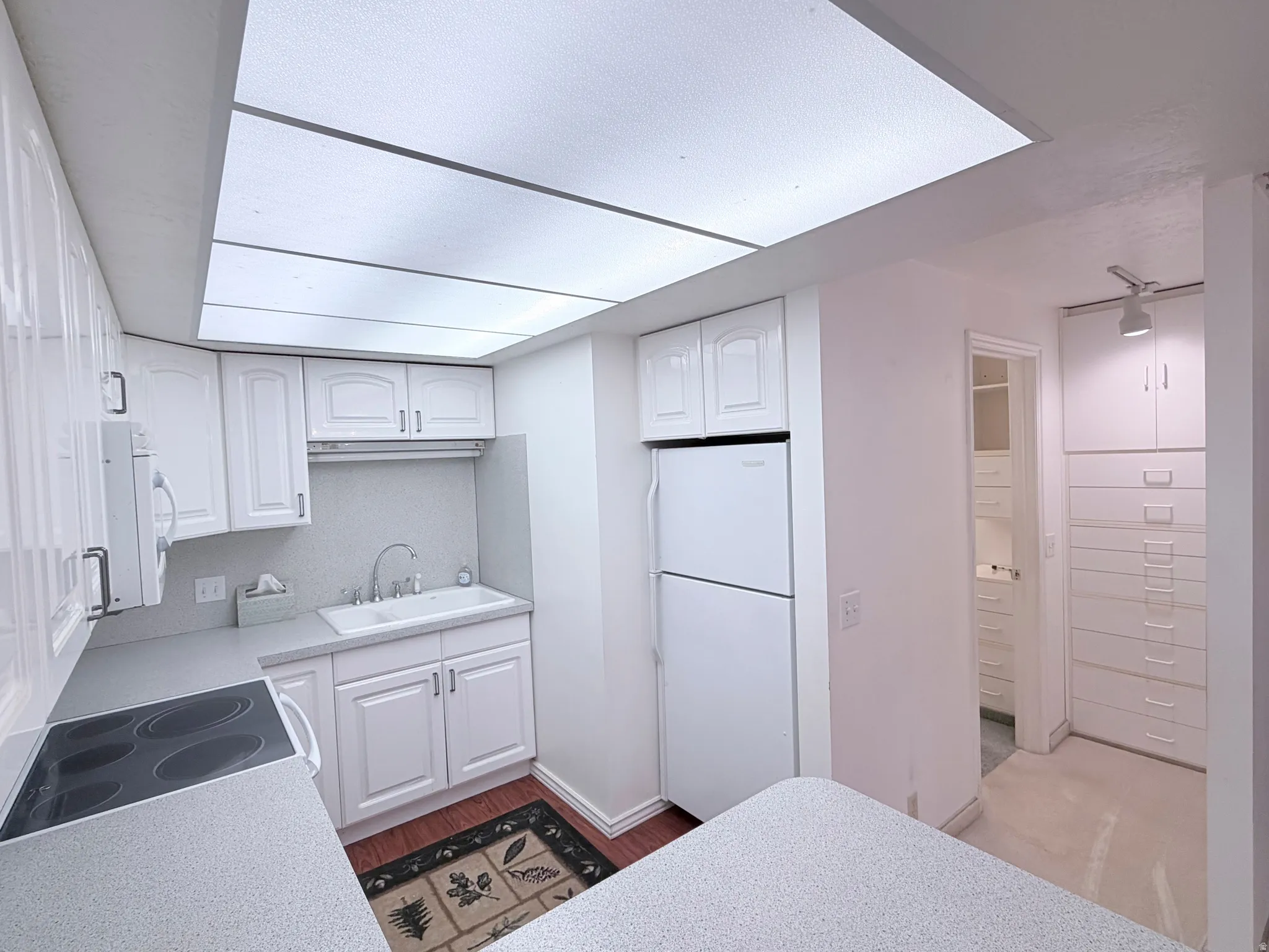 Kitchen featuring white cabinets, light countertops, white appliances, and dark wood-style floors