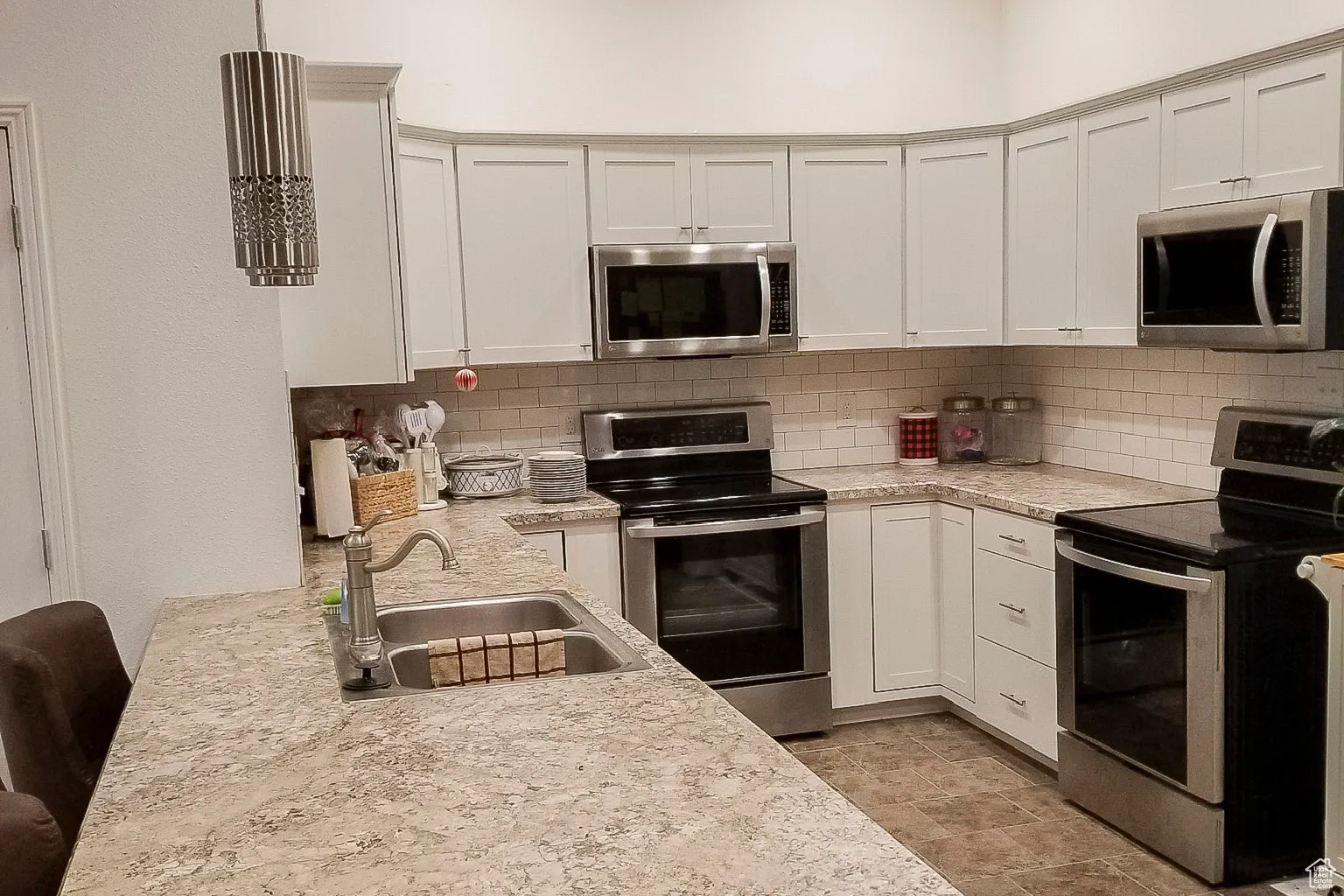 Kitchen featuring stainless steel appliances, decorative backsplash, white cabinetry, and light stone counters