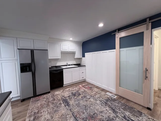 Kitchen featuring a barn door, white cabinets, dark countertops, stainless steel fridge, and dishwasher