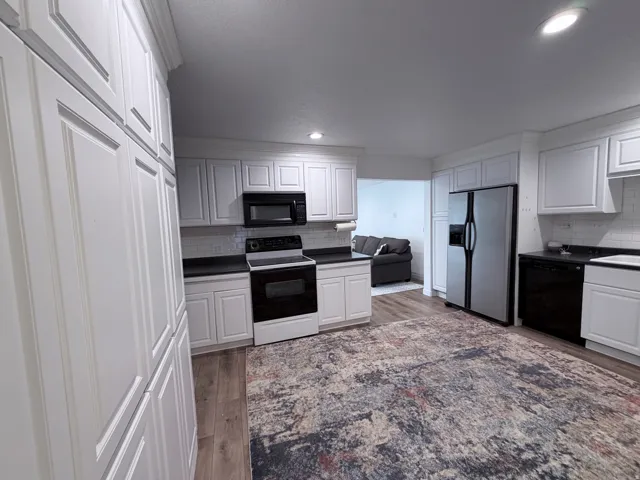 Kitchen with black appliances, white cabinetry, light wood-style flooring, tasteful backsplash, and recessed lighting