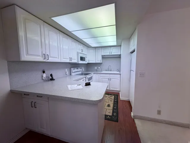 Kitchen featuring white cabinetry, a peninsula, light countertops, white appliances, and dark wood-style flooring