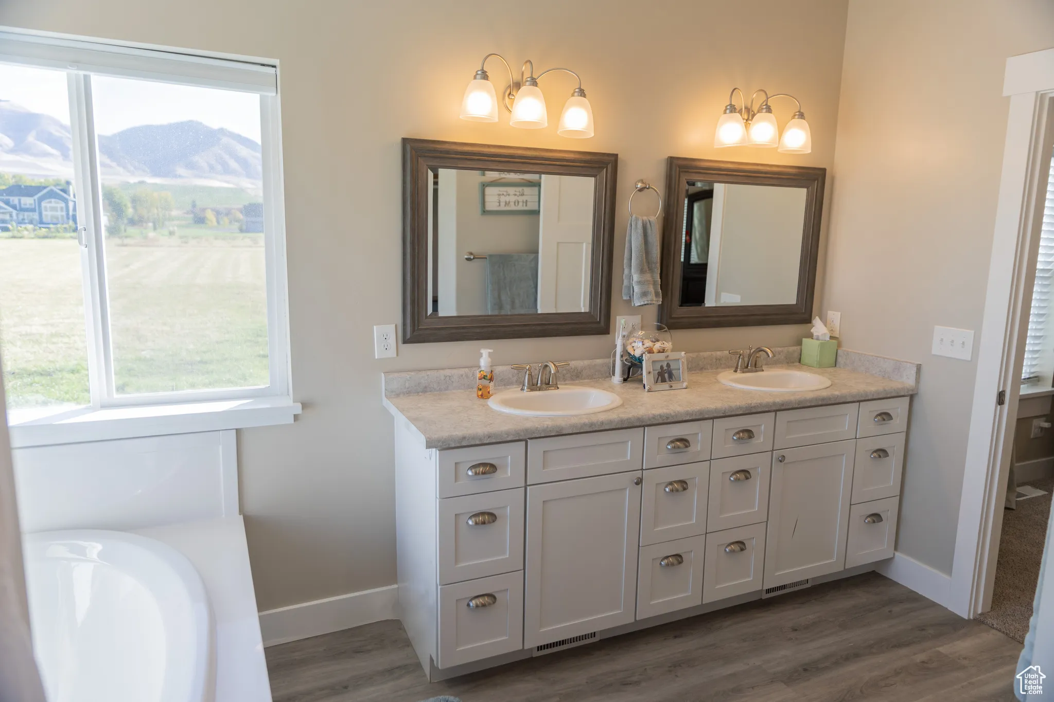 Master bathroom featuring double vanity, dark wood LVP floors, and a bath