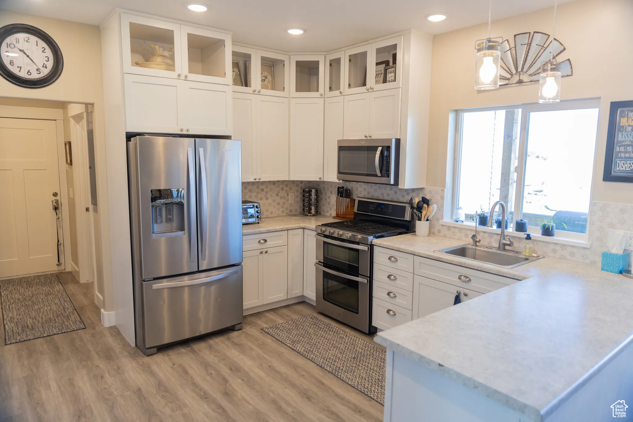 Kitchen featuring pendant lighting, appliances with stainless steel finishes, light countertops, white cabinetry, and tasteful tiled backsplash