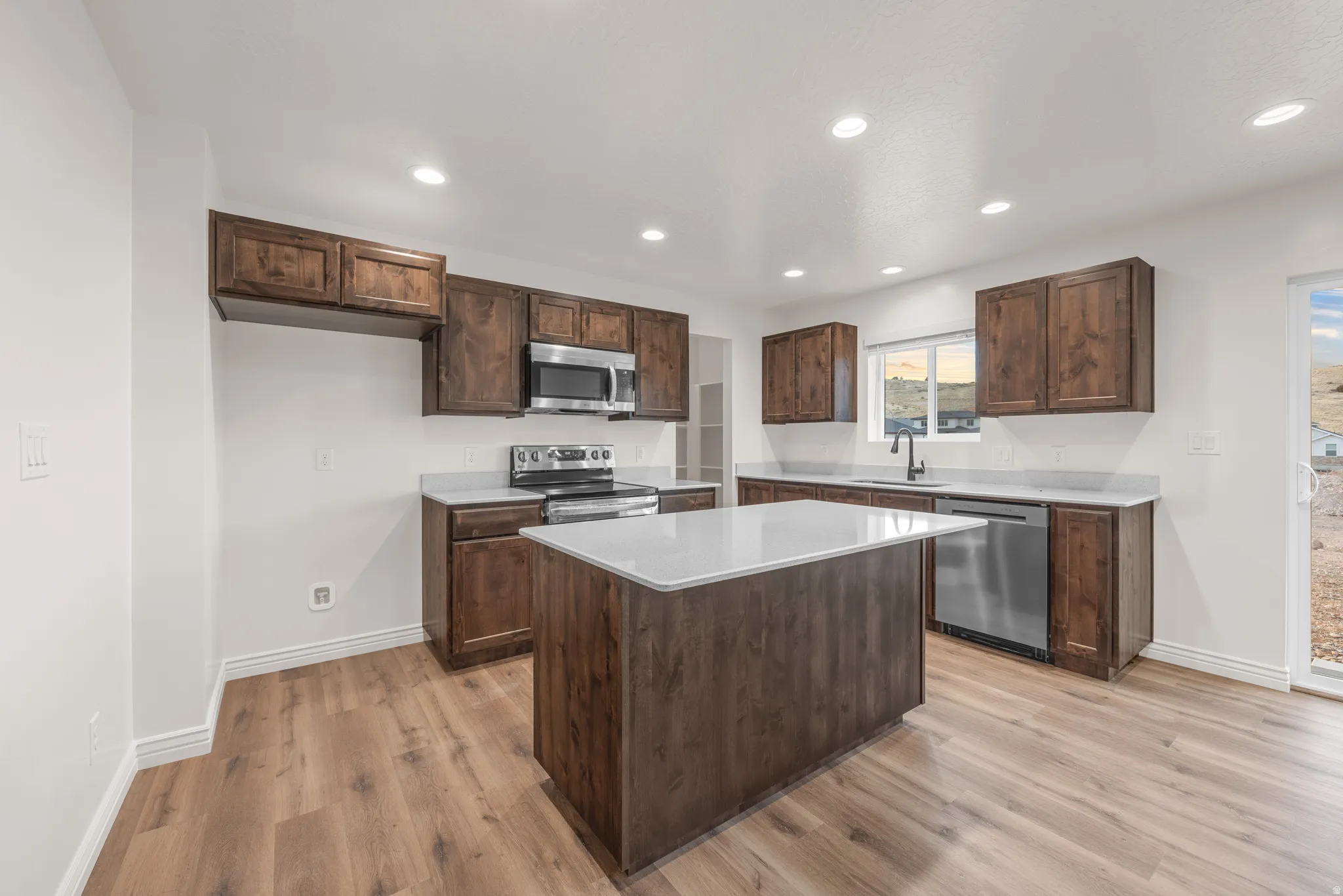 Kitchen with dark wood finish cabinets, stainless steel appliances, a center island, light wood-style flooring, and recessed lighting