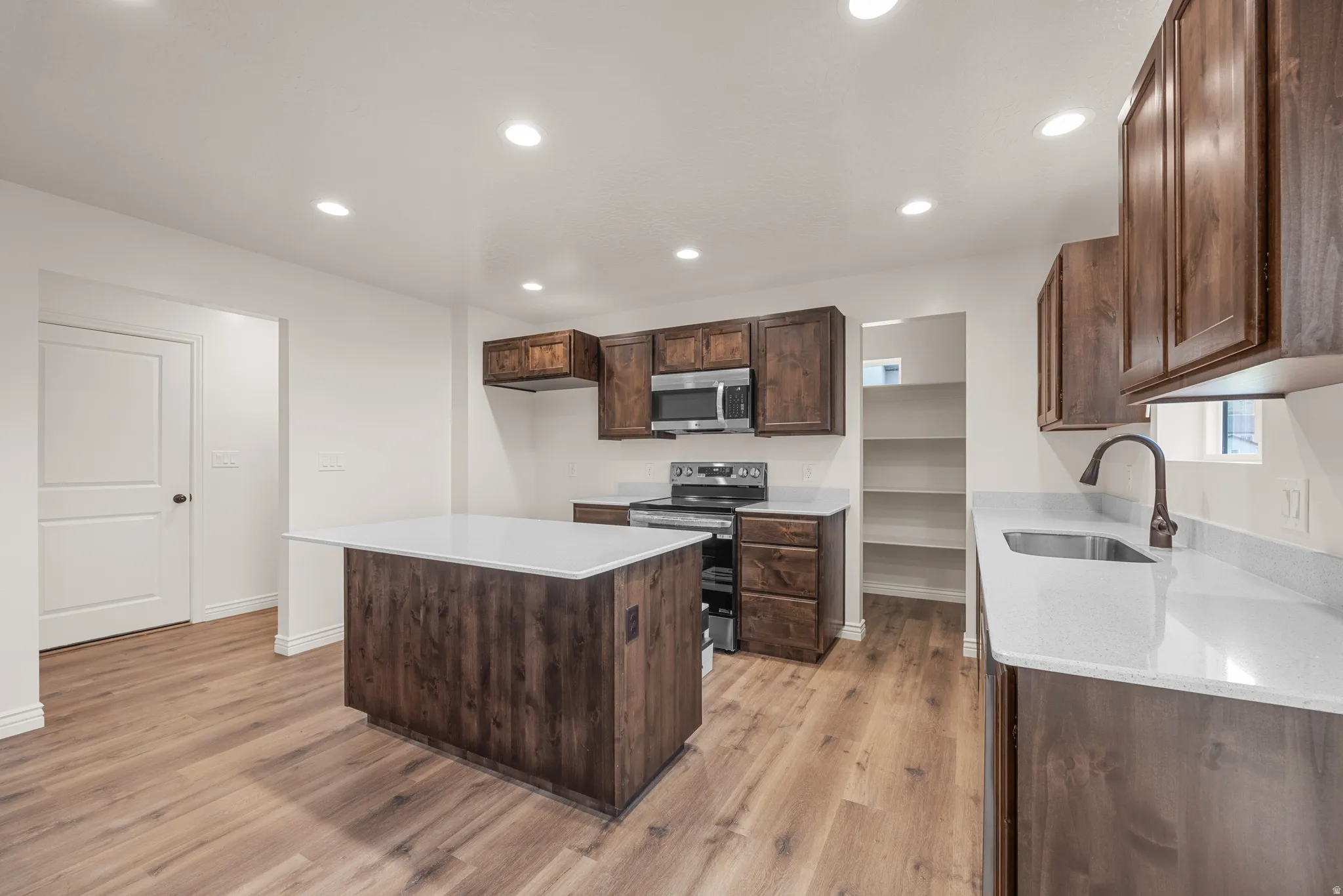 Kitchen featuring stainless steel appliances, dark wood finish cabinetry, a center island, light stone counters, and recessed lighting