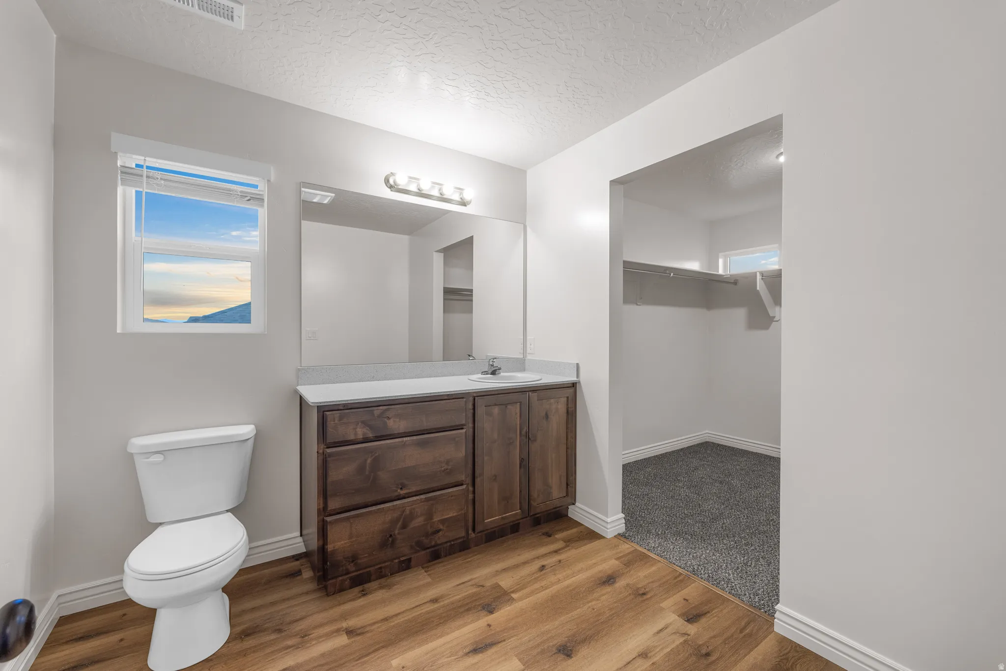 Bathroom with a textured ceiling, vanity, light wood-style floors, and a spacious closet