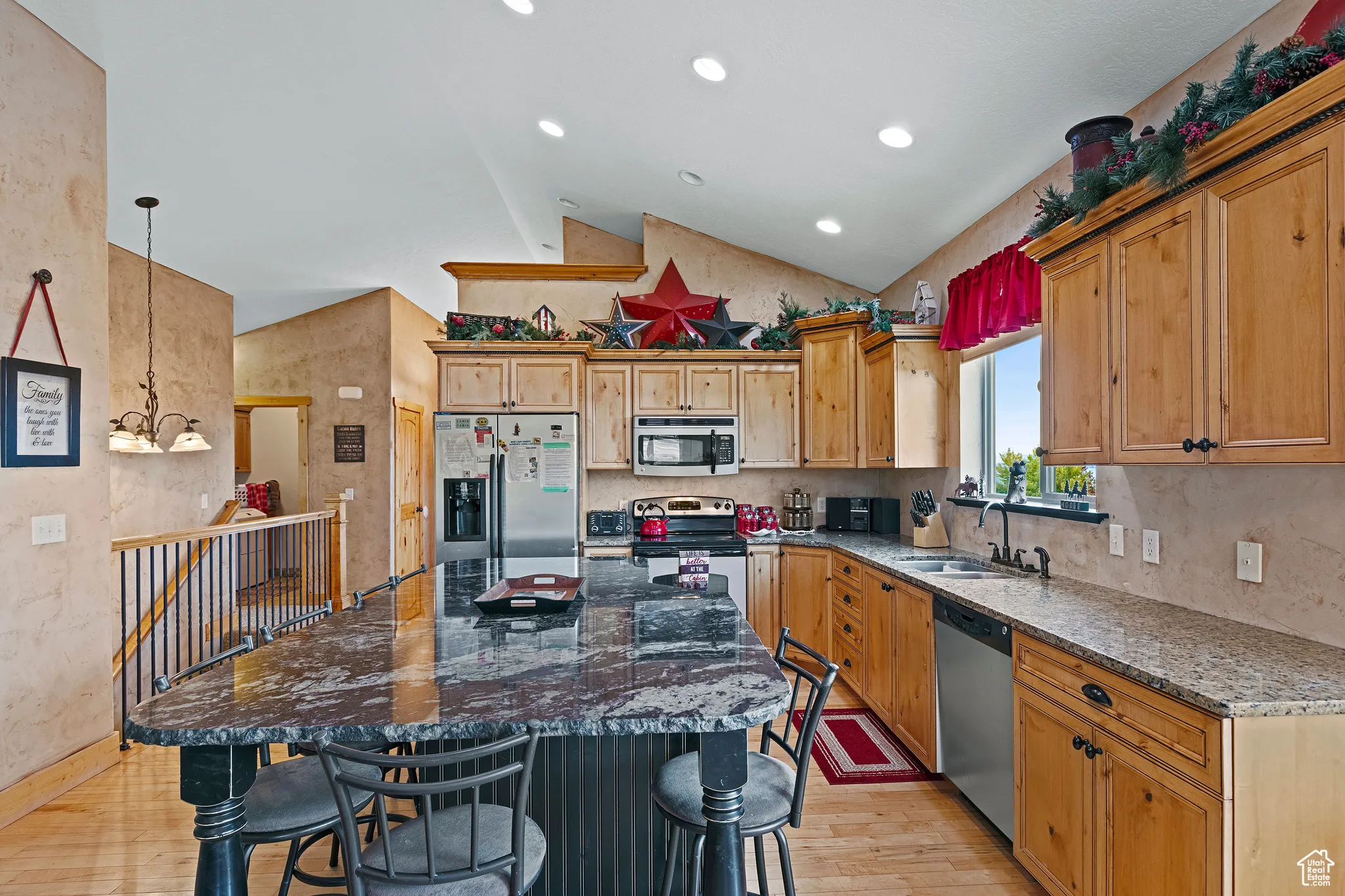 Kitchen with dark stone counters, light wood-style flooring, stainless steel appliances, lofted ceiling, and hanging light fixtures