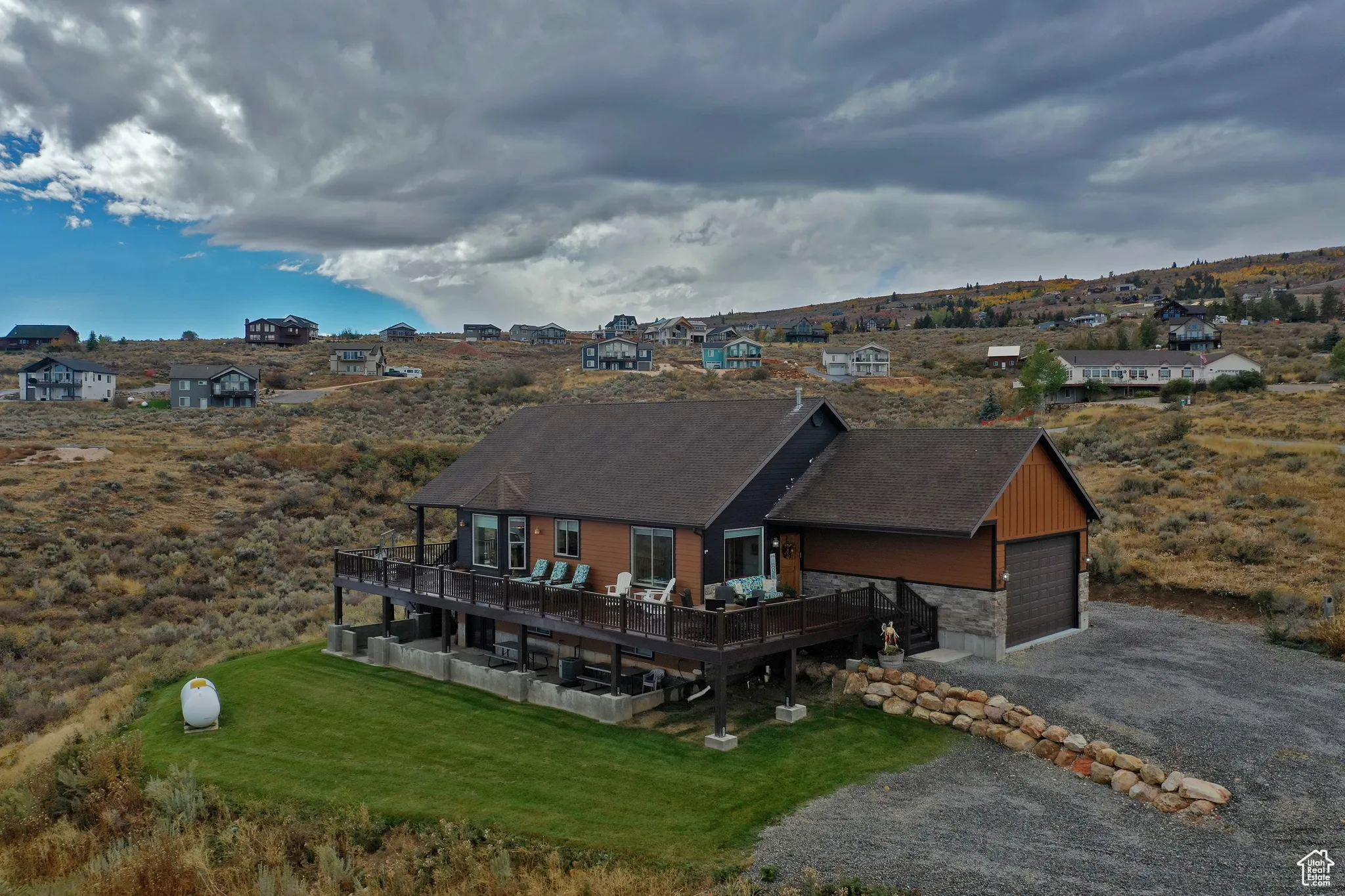 View of front of home featuring stone siding, a wooden deck, driveway, and a front lawn