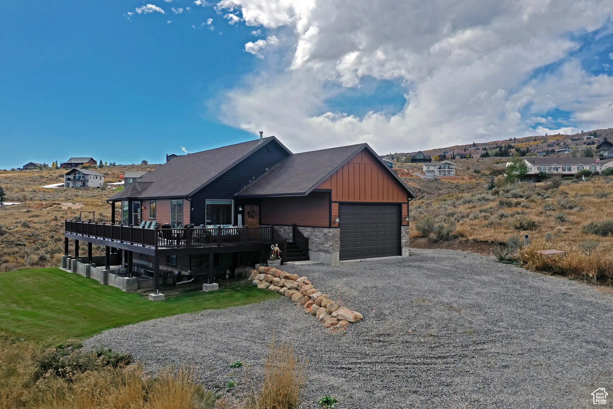 View of front of property featuring a wooden deck, gravel driveway, stone siding, board and batten siding, and a garage