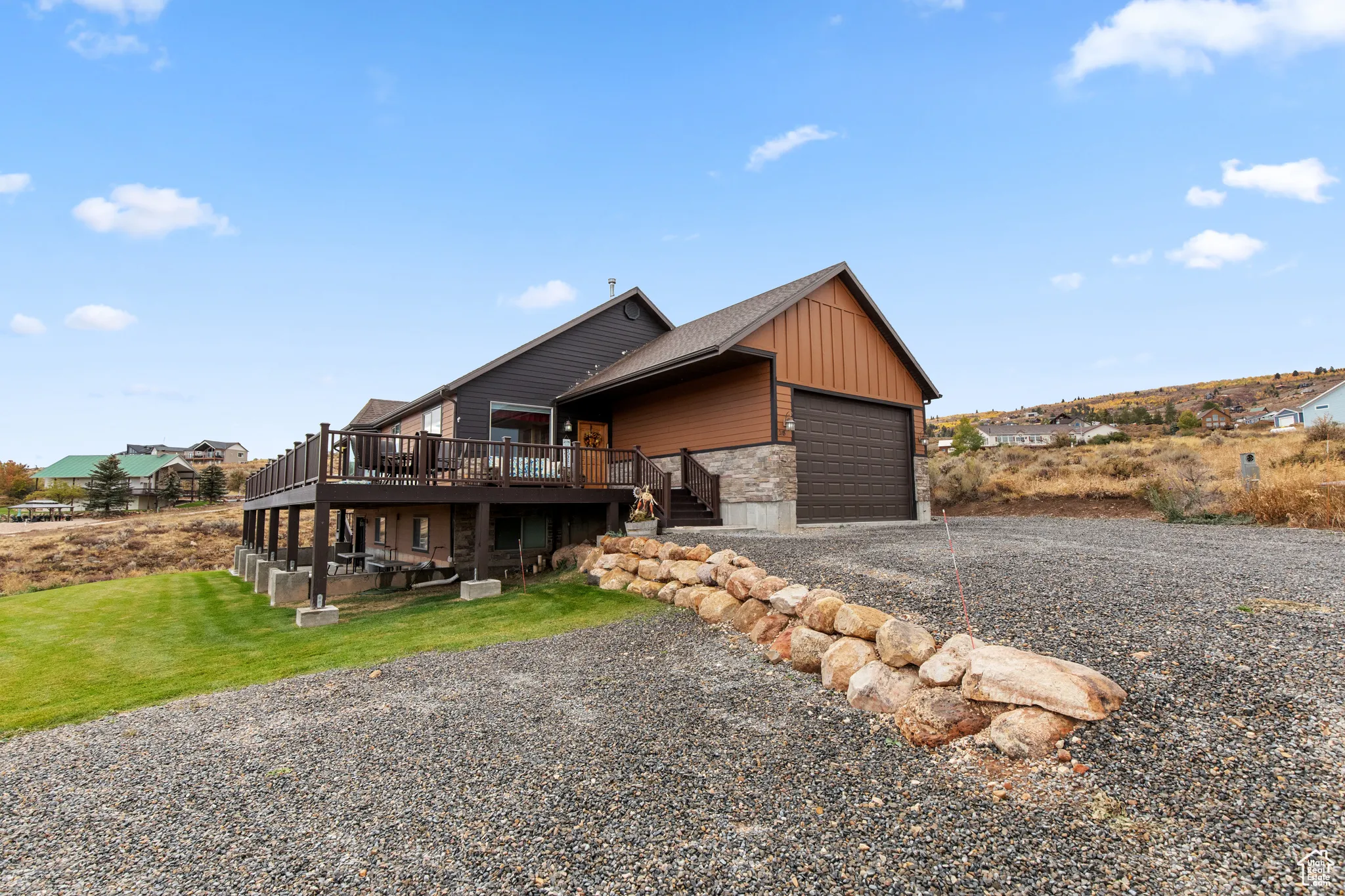 View of side of home featuring a wooden deck, stone siding, gravel driveway, stairs, and a yard