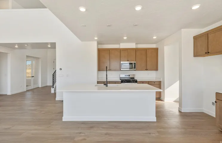 Kitchen featuring brown cabinets, an island with sink, light wood finished floors, stainless steel appliances, and recessed lighting