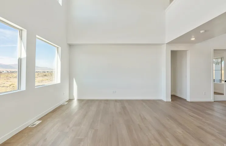 Unfurnished room featuring a high ceiling, light wood-style flooring, plenty of natural light, and a mountain view