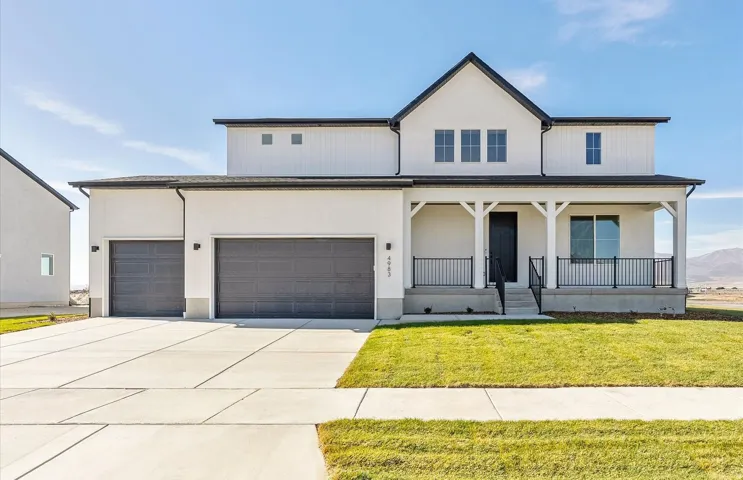 Modern farmhouse style home featuring a porch, a front lawn, driveway, stucco siding, and a garage