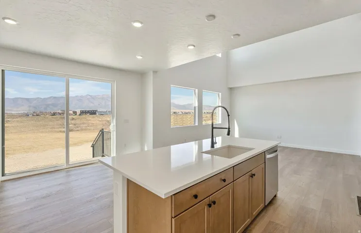 Kitchen with brown cabinetry, light wood-type flooring, a kitchen island with sink, plenty of natural light, and a textured ceiling
