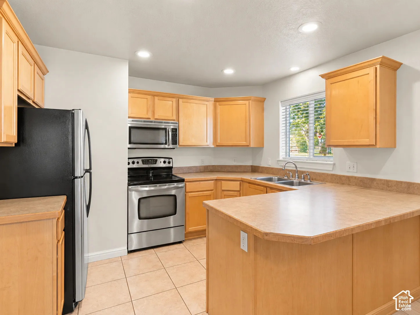 Kitchen featuring natural wood cabinetry, laminate countertops, stainless steel appliances, tile flooring, and recessed lighting