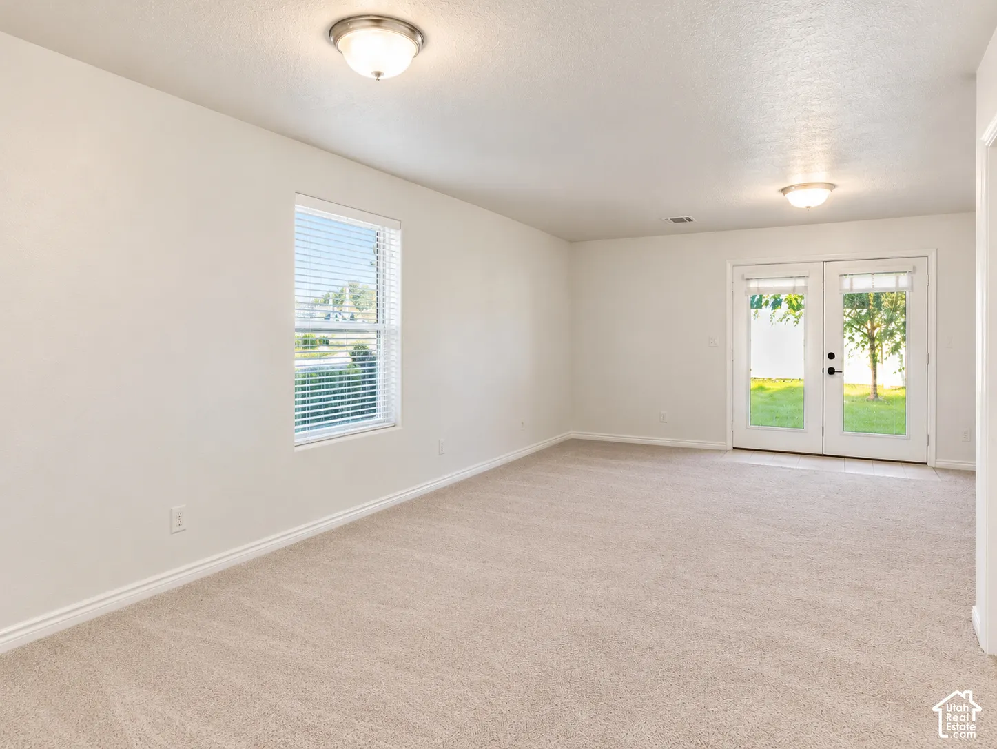 Neutral wall-to-wall carpeting, dual flush-mount ceiling light fixtures, single-hung window, and glass-paned double doors