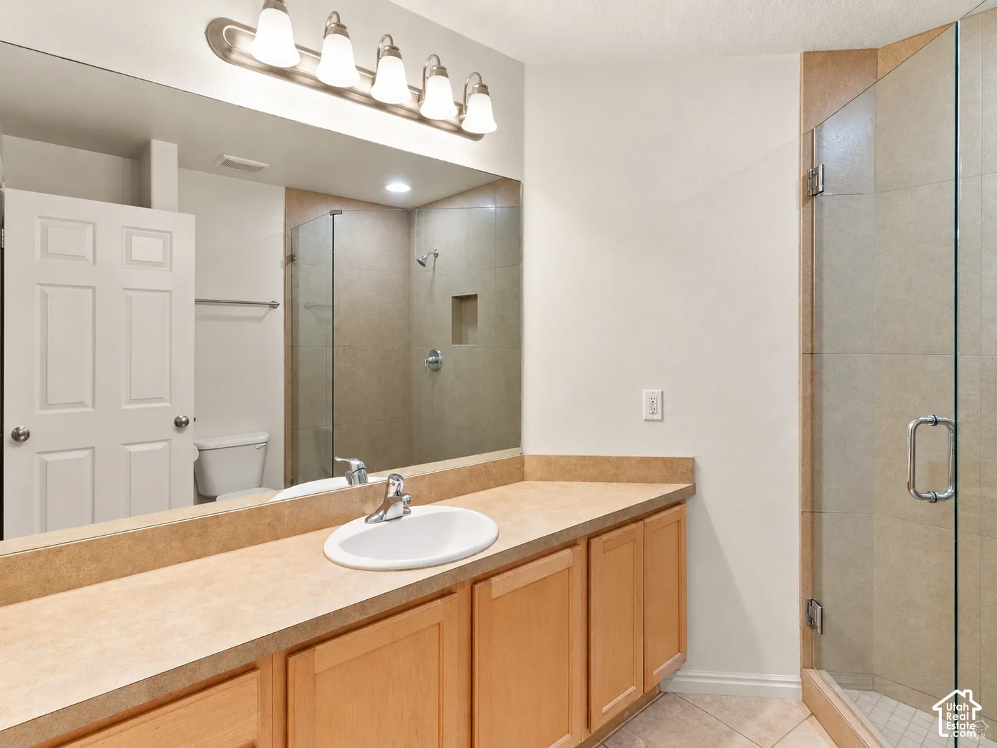 Full-width vanity with a solid-surface countertop and integrated backsplash, undermount sink, multi-light fixture, and walk-in shower with a glass enclosure